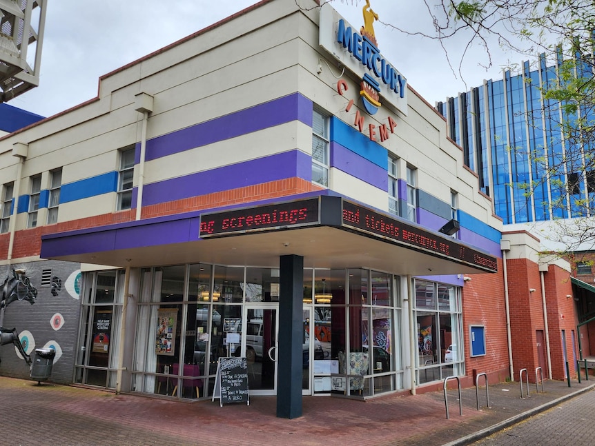 An old cinema with purple and brick walls with signs out the front 