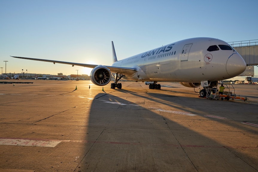 A plane with qantas down the side sitting on the tarmac with the sun rising behind it