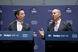 Two men in suits stand in front of podiums and banners marketing the 2021 budget, with Australian flags standing on either side.
