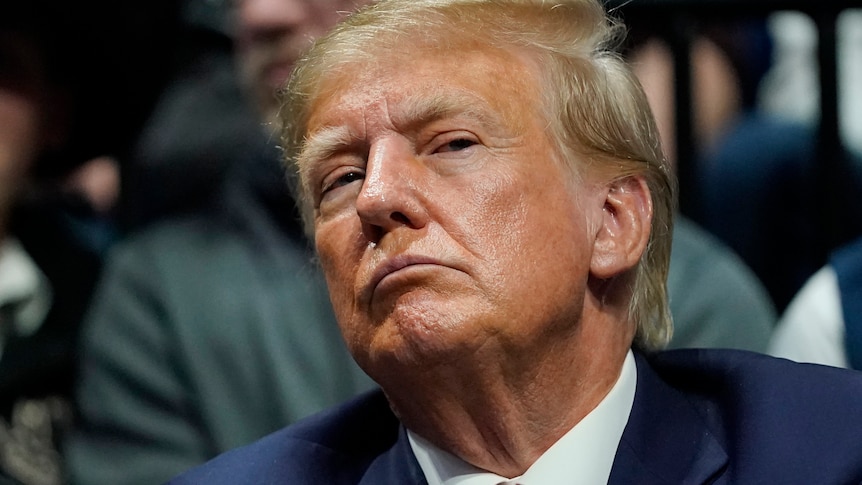 A close up of Donald Trump wearing a suit with a red tie, with a look of concentration on his face