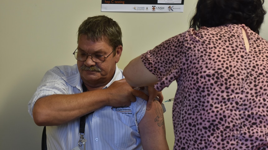 Man holds shirt up while vaccination needle is stuck into arm