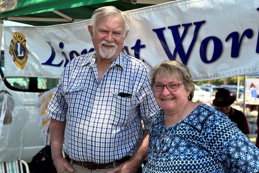 Photo of an older man with white hair and a middle-aged woman with glasses in front of a gazebo with a sign 'Lions at work'
