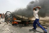An Iraqi teenager throws a rock at a burning vehicle