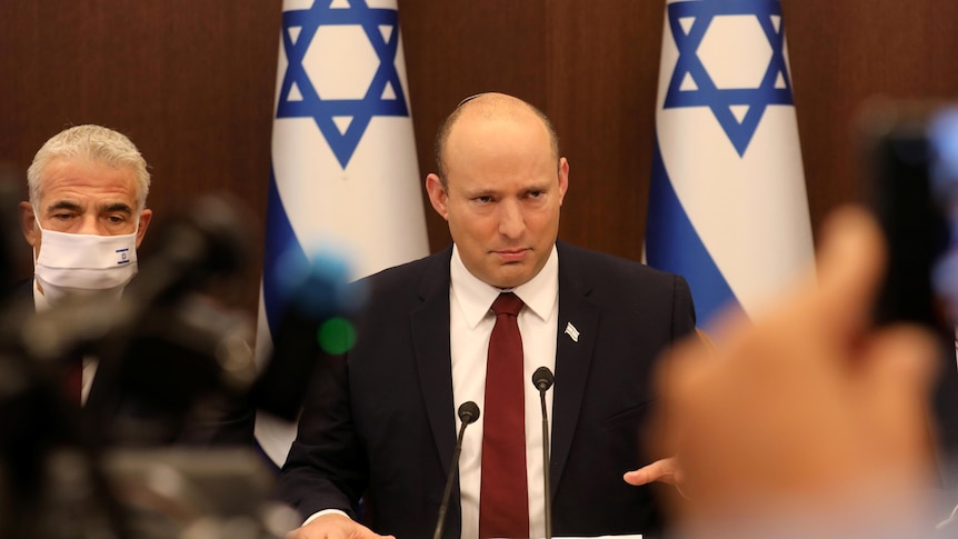 Naftali Bennett sitting at a table in front of Israeli flags.