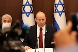 Naftali Bennett sitting at a table in front of Israeli flags.