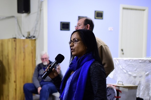 An Aboriginal woman stands in front of a crowd in a room with a microphone in her hand.