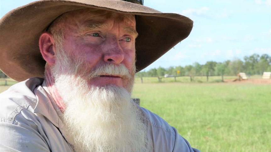 a man with a hat on stands on a property, looking at the road in the distance