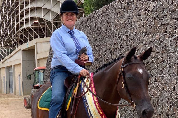 Andy Dobson sitting on her horse holding a trophy