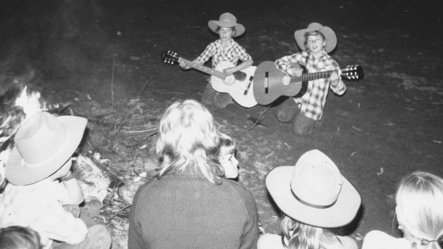 MLis and Tanya with guitars in creekbed around fire at camp