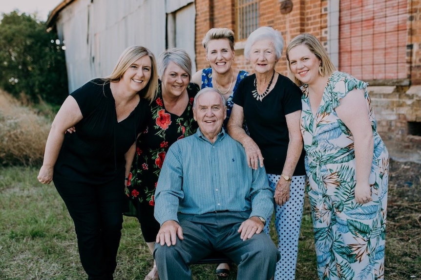 A seated man surrounded by 5 standing women