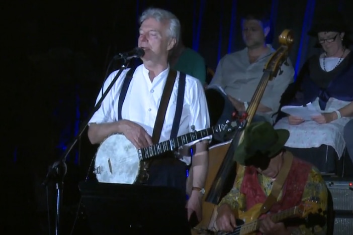 A man stands on a stage, playing guitar and singing.