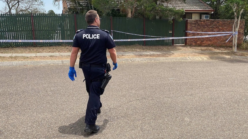 A police officer walks towards a house with police tape outside it.
