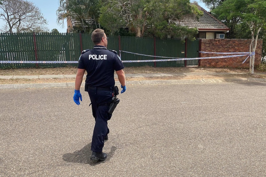 A police officer walks towards a house with police tape outside it.