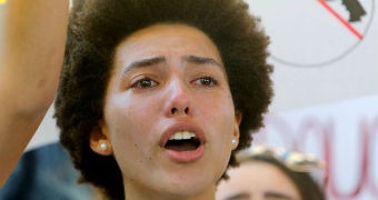 A woman cries and stands in front of a sign of a gun with a cross through it.