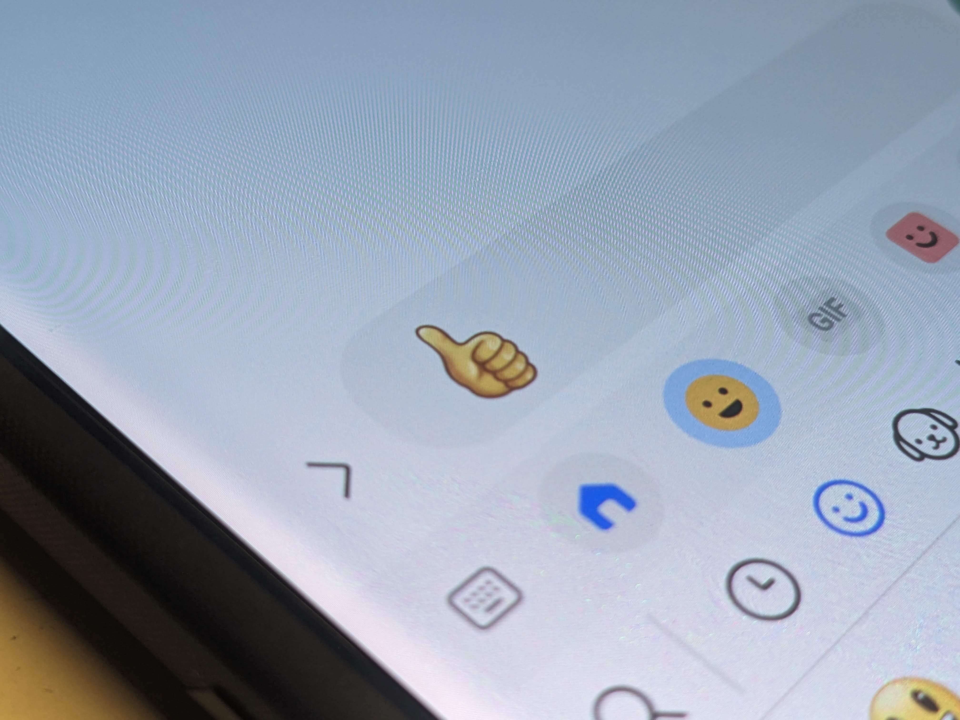 A photo of a phone displaying a thumbs up emoji in a text message box