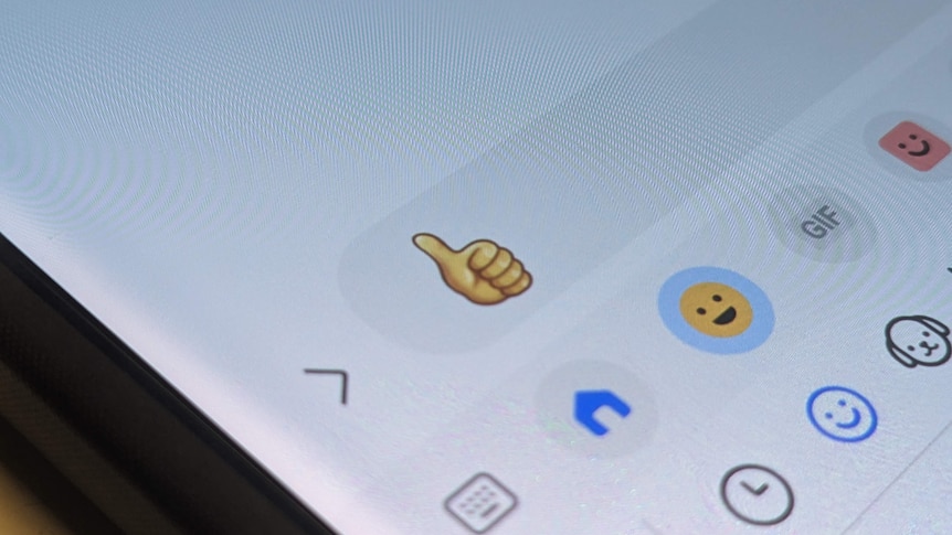 A photo of a phone displaying a thumbs up emoji in a text message box