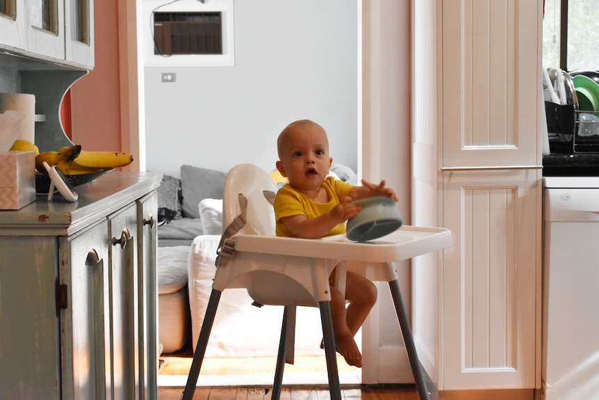 A child in a high chair holding an empty bowl