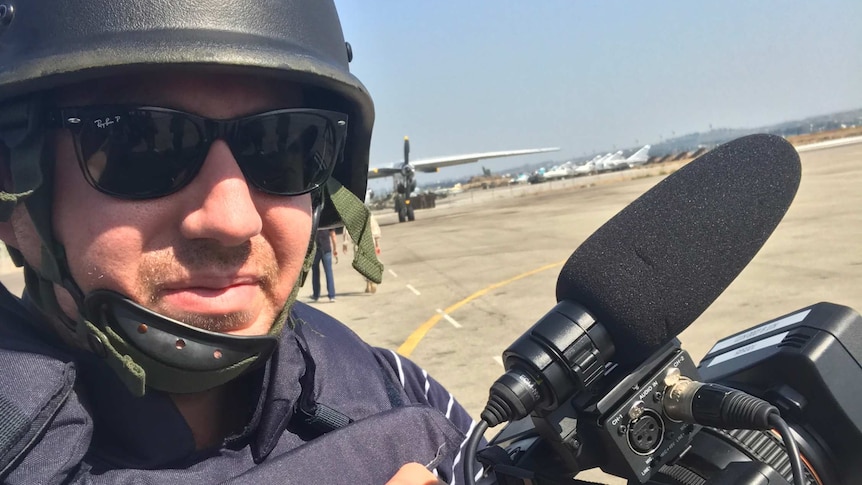 A cameraman wears a helmet and Press vest on a runway