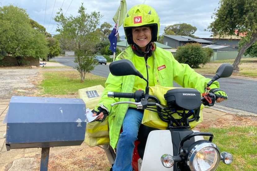 A postie in yellow high-vis gear smiles as she posts a letter