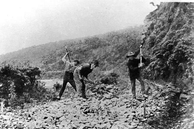 A black and white photo of three men with tools building a road.