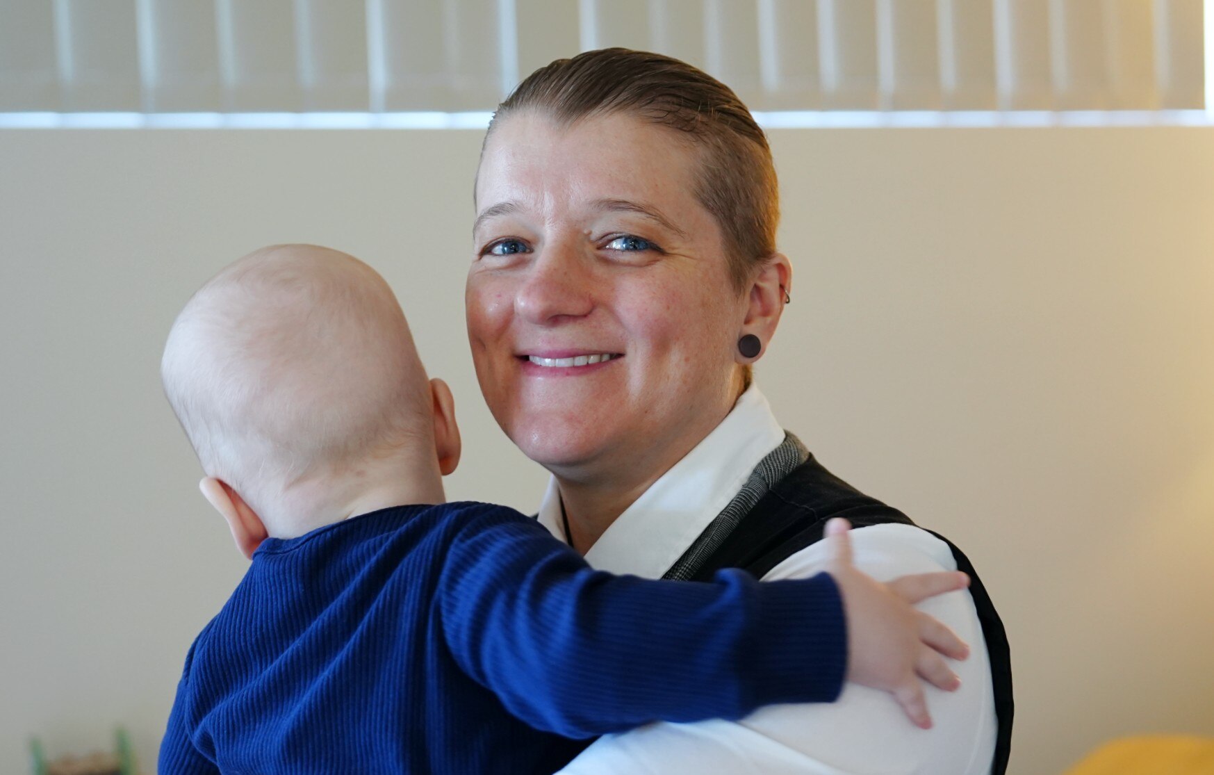 Una toma de cabeza y hombros de una mujer sonriente sosteniendo a un bebé con el rostro vuelto hacia la cámara.
