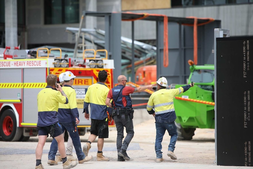 Workers in hi-vis clothing walk alongside a police officer near a fire truck at a construction site.