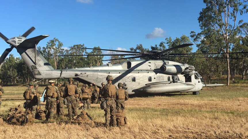 Troops walk towards a US helicopter with bushland in the background