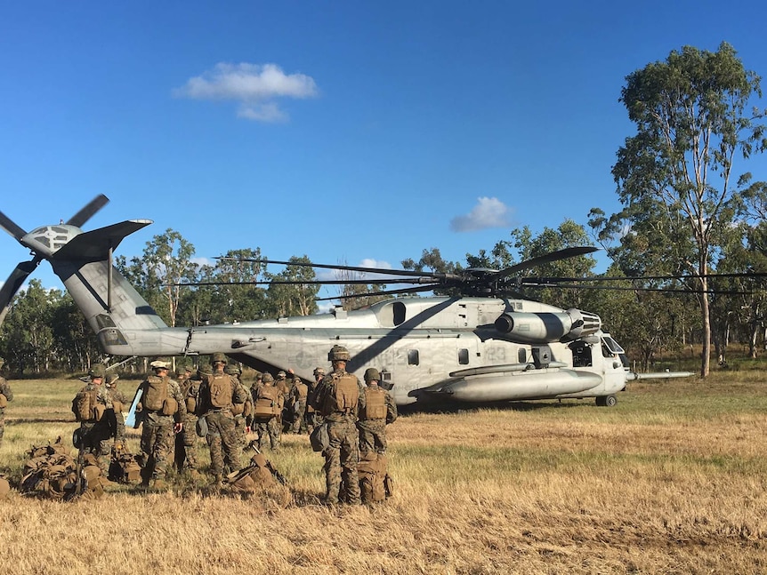 Troops walk towards a US helicopter with bushland in the background