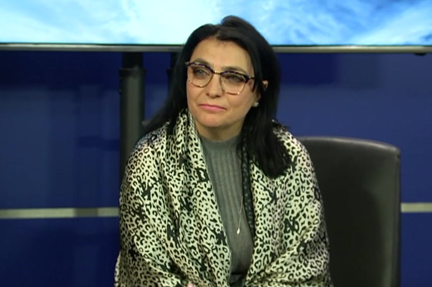 A woman with black hair, glasses and a leopard print scarf speaks at a police press conference.