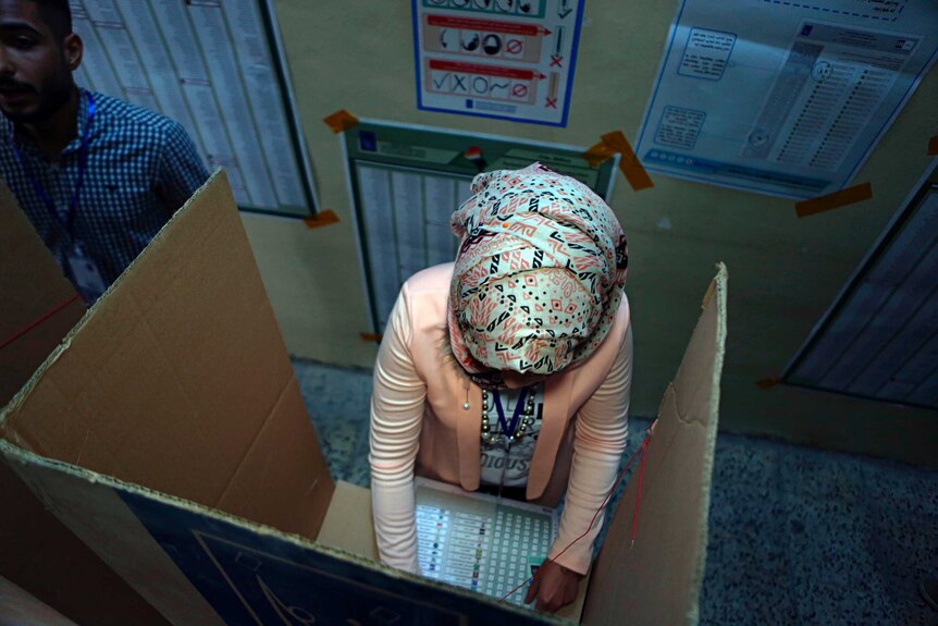 An Iraqi woman casts her vote in a cardboard ballot box