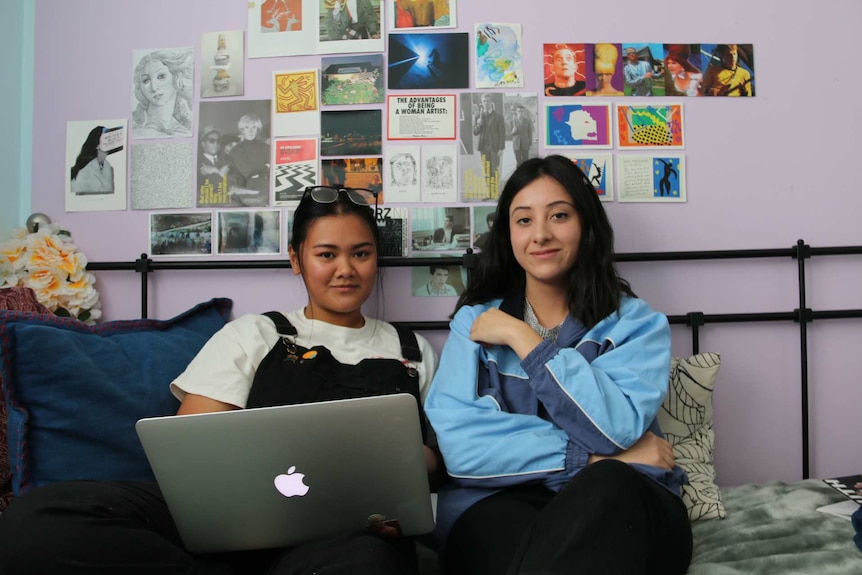 Jennifer Andrade and Jade Diaz sit on bed with laptop.