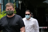 A man in a black shirt and green face mask and a man with dark hair and sunglasses in a white shirt