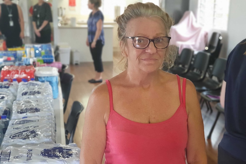 A middle aged woman stands in front of donated items. The close up photo captures her fatigue.