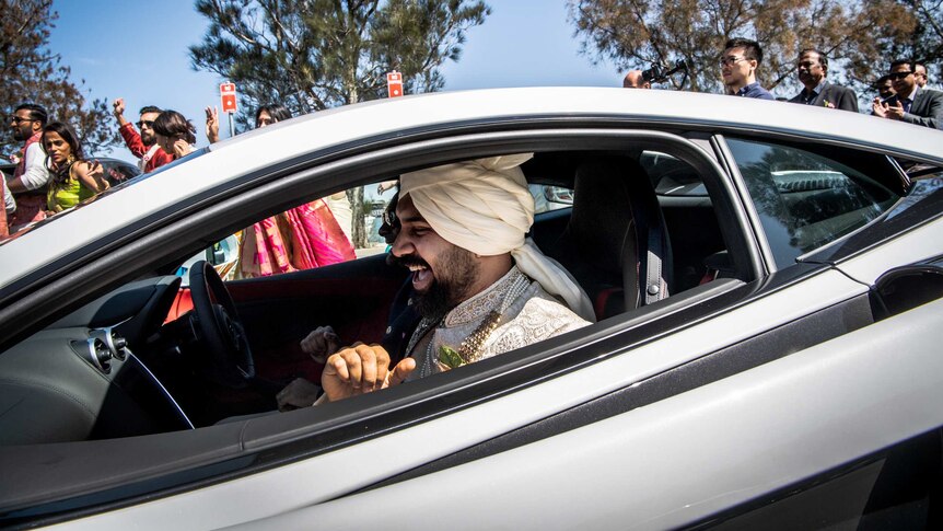 A man with traditional Indian dress sits in the front passenger seat of a sports car.