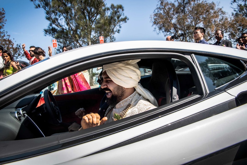 A man with traditional Indian dress sits in the front passenger seat of a sports car.