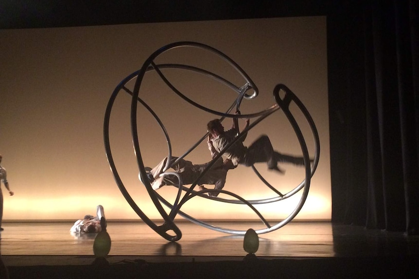 Acrobats on a wheel-like piece of circus equipment on stage.