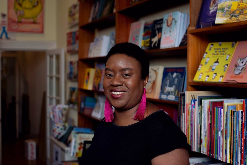 The writer Maxine Beneba Clarke standing in front a bookshelf of children's books in a bookstore
