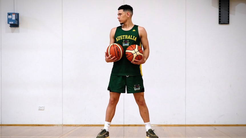 Jarrod, wearing a green Australia jersey, stands confidently with a basketball in each hand while looking to the side.