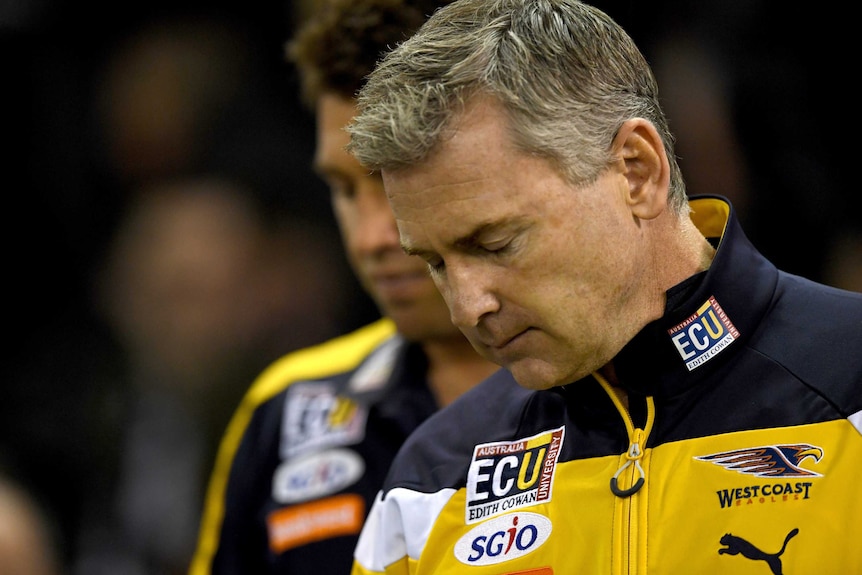 A tight head and shoulders shot of Adam Simpson with his eyes closed and his head bowed wearing an Eagles jacket.