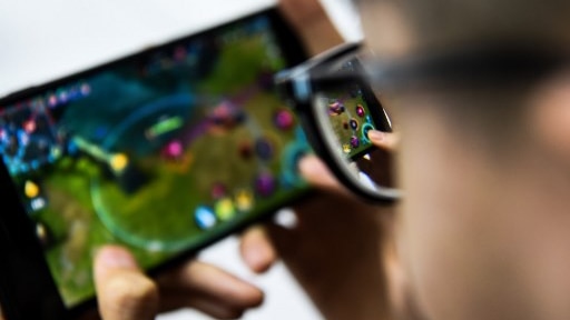 A man with glasses plays a video game on a phone.