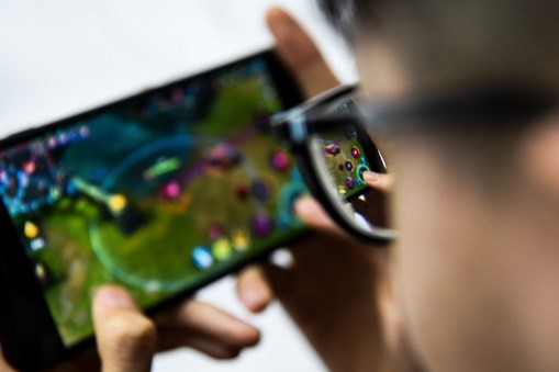 A man with glasses plays a video game on a phone.