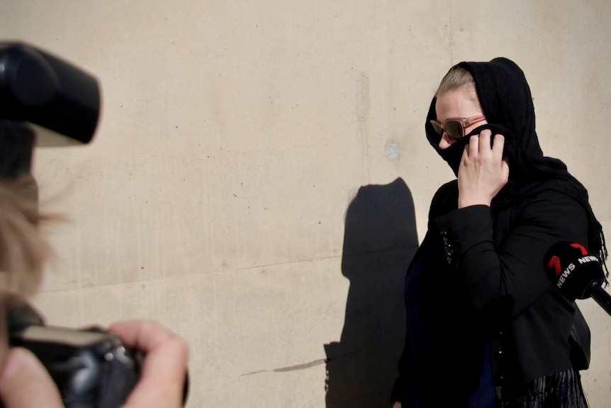 a woman covering her face and head with a black scarf, wearing sun glasses as she leaves court
