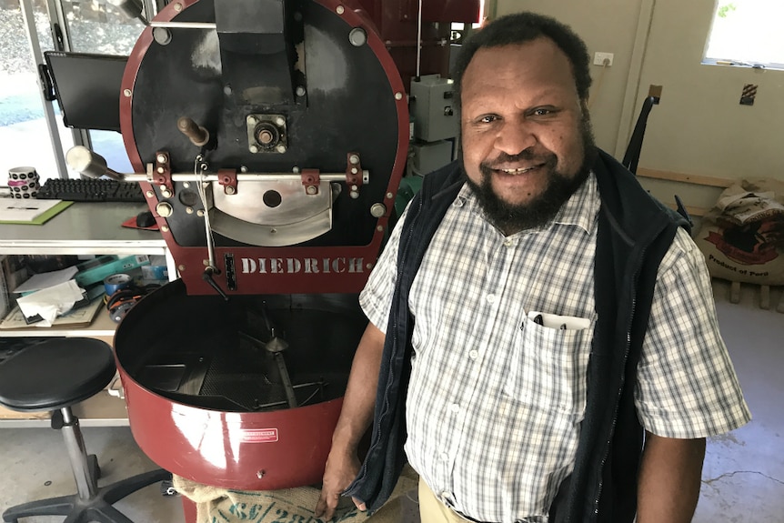Daniel Kinne next to a coffee roaster and a bag of PNG coffee beans.