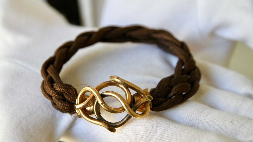 A bracelet made from brown human hair, with a gold infinity knot clasp