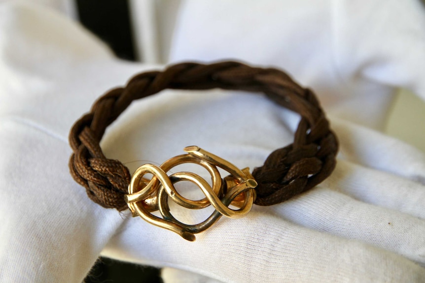 A bracelet made from brown human hair, with a gold infinity knot clasp