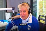 australian radio presenter Ron E Sparks sits behind a microphone with headphones on looking at the camera