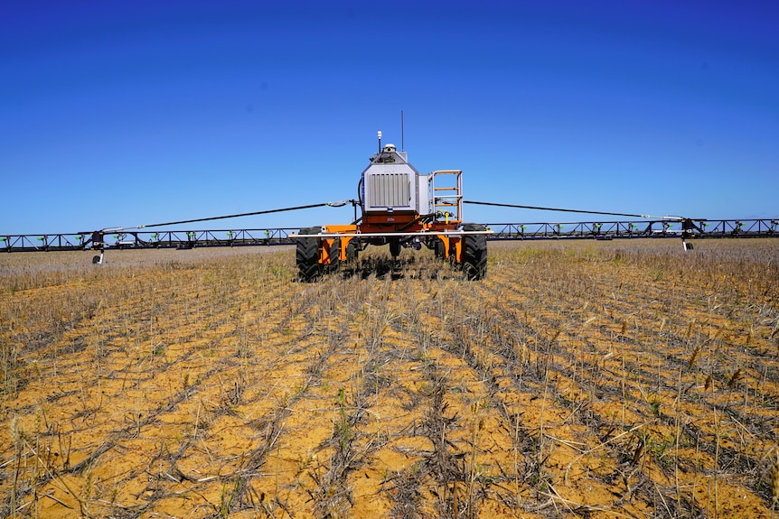 A front on picture of a robotic sprayer on land with stubble, blue skies.