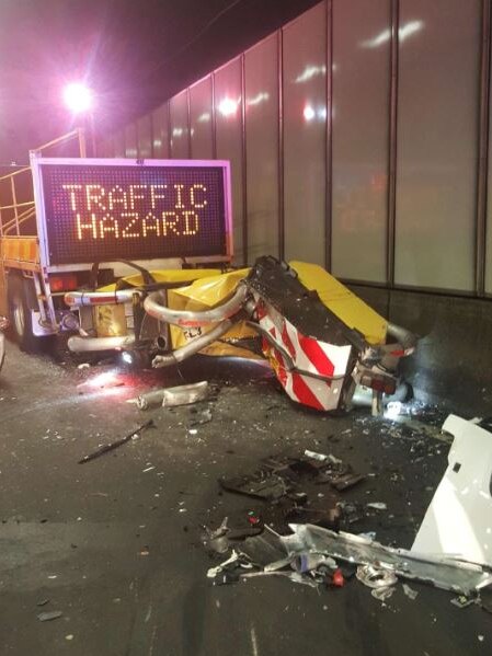 Part of a smashed car sit in front of the traffic hazard warning sign.