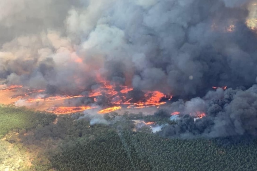 A photo from the air shows masses of dark smoke clouds hovering over an active yellow and red flamed fireground.