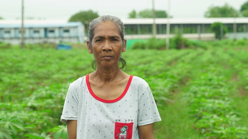 A woman standing in a field with a factory behind her